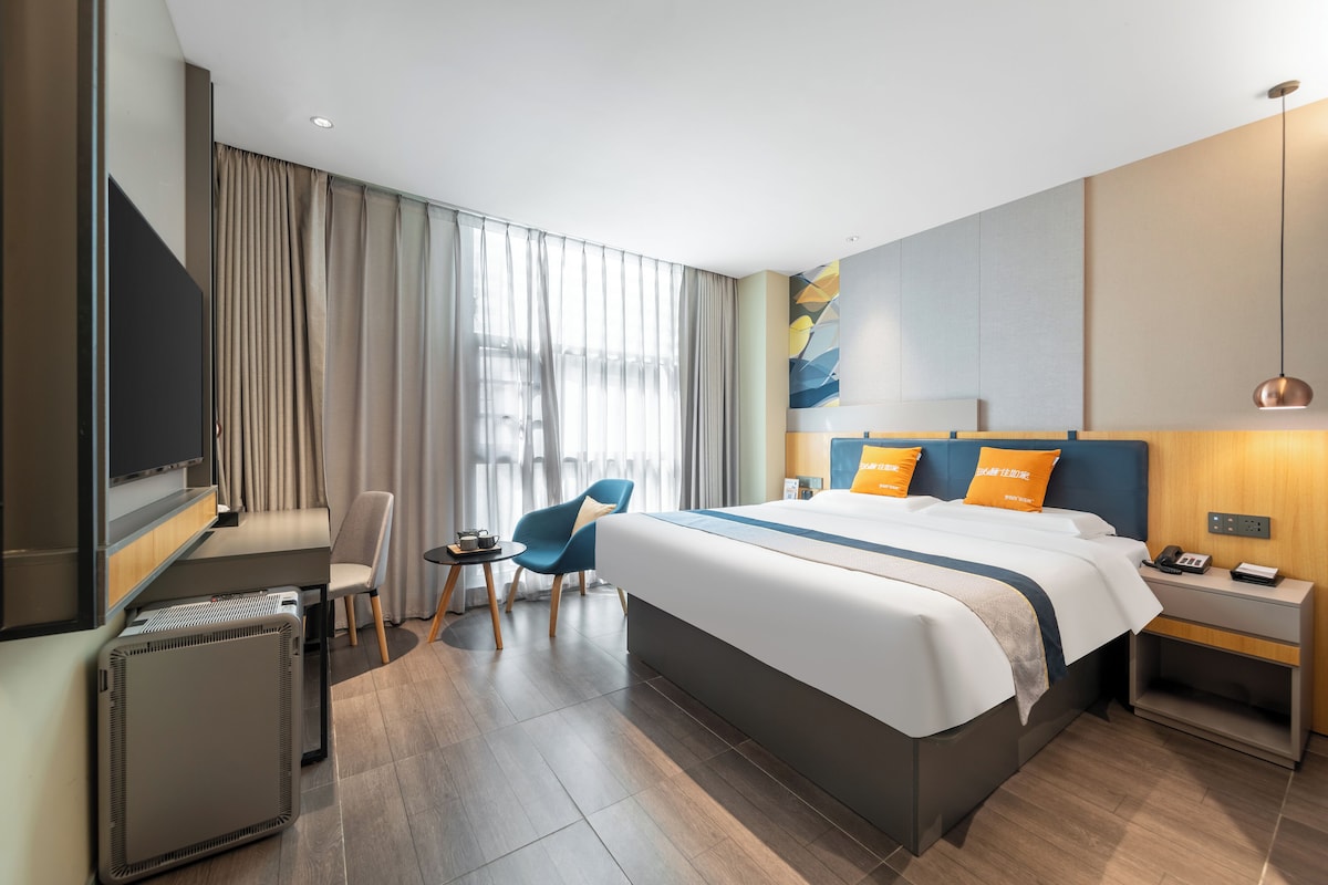 A modern hotel room with a large bed, a desk, a chair, and a TV.