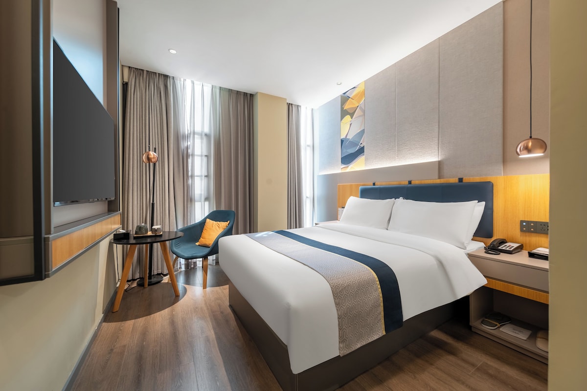 A hotel room with a large bed, a desk with a phone, a chair, and a TV.