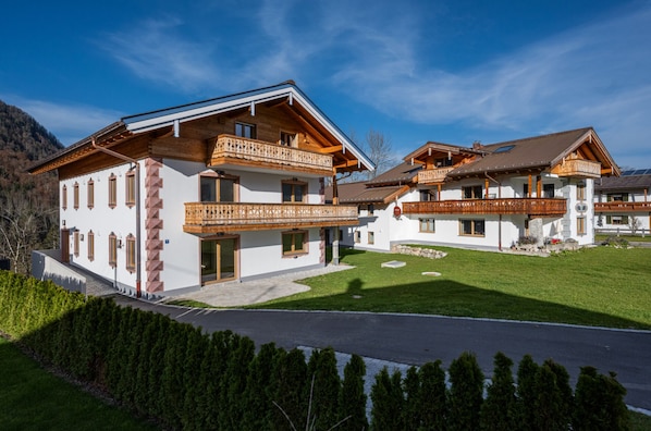 A two-story chalet with wooden balconies, white walls, and a clear sky.