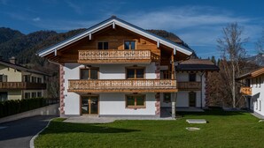 Eine zweistöckige Chalet mit Holzbalkon, einem Kiesweg und einem Berg im Hintergrund.