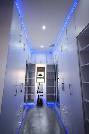 A narrow hallway with a vacuum cleaner, shelves, and blue LED lighting.