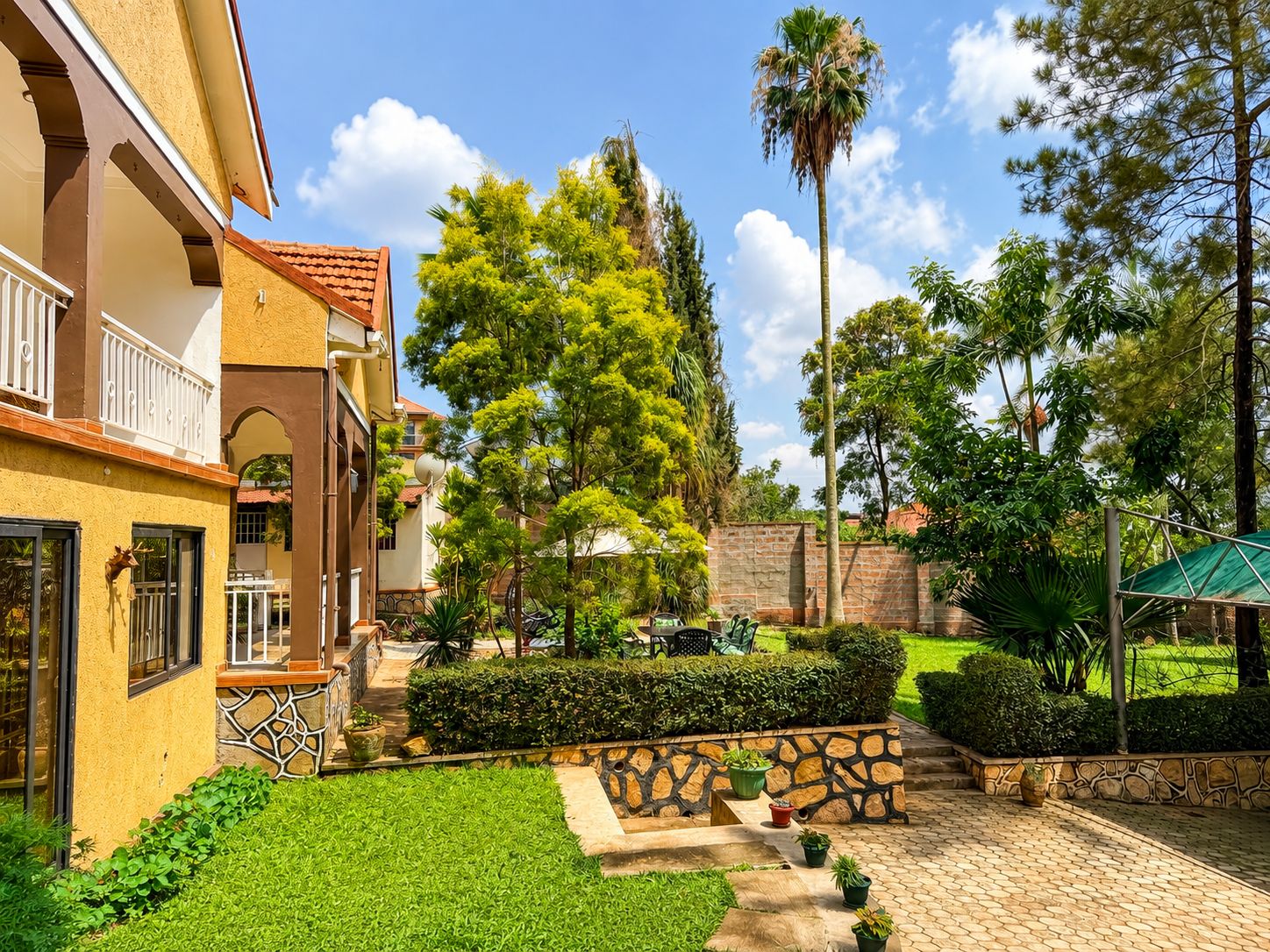 A courtyard with a paved walkway, a palm tree, and a building with a balcony.