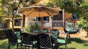 An outdoor patio with a table and chairs, surrounded by greenery and a building with a balcony. - Vista Palms Retreat 3 bed and 2 bath Private Hilltop house in Bunamwaya Kampala. (Kampala)