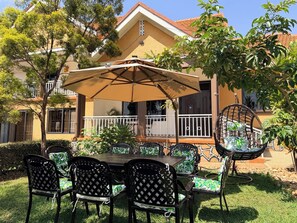 An outdoor patio with a table and chairs, surrounded by greenery and a building with a balcony. - Vista Palms Retreat 3 bed and 2 bath Private Hilltop house in Bunamwaya Kampala. (Kampala)