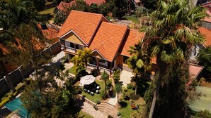 A two-story house with a red-tiled roof, surrounded by greenery and a small patio area. - Vista Palms Retreat 3 bed and 2 bath Private Hilltop house in Bunamwaya Kampala. (Kampala)