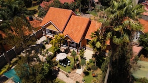 A two-story house with a red-tiled roof, surrounded by greenery and a small patio area. - Vista Palms Retreat 3 bed and 2 bath Private Hilltop house in Bunamwaya Kampala. (Kampala)