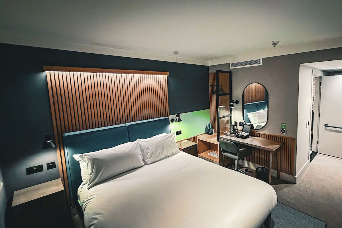 A hotel room with a bed, desk, and a mirror.