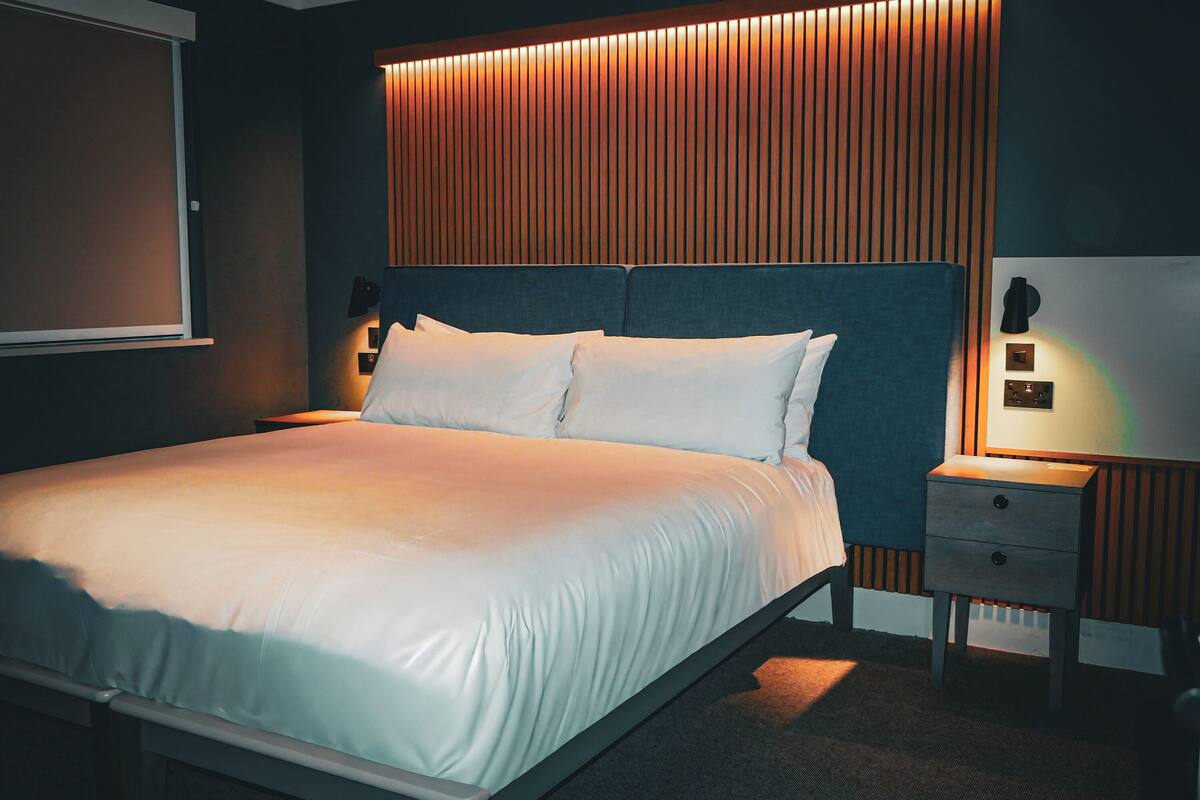 A neatly made bed with white linens, a wooden headboard, and a bedside table with a lamp.