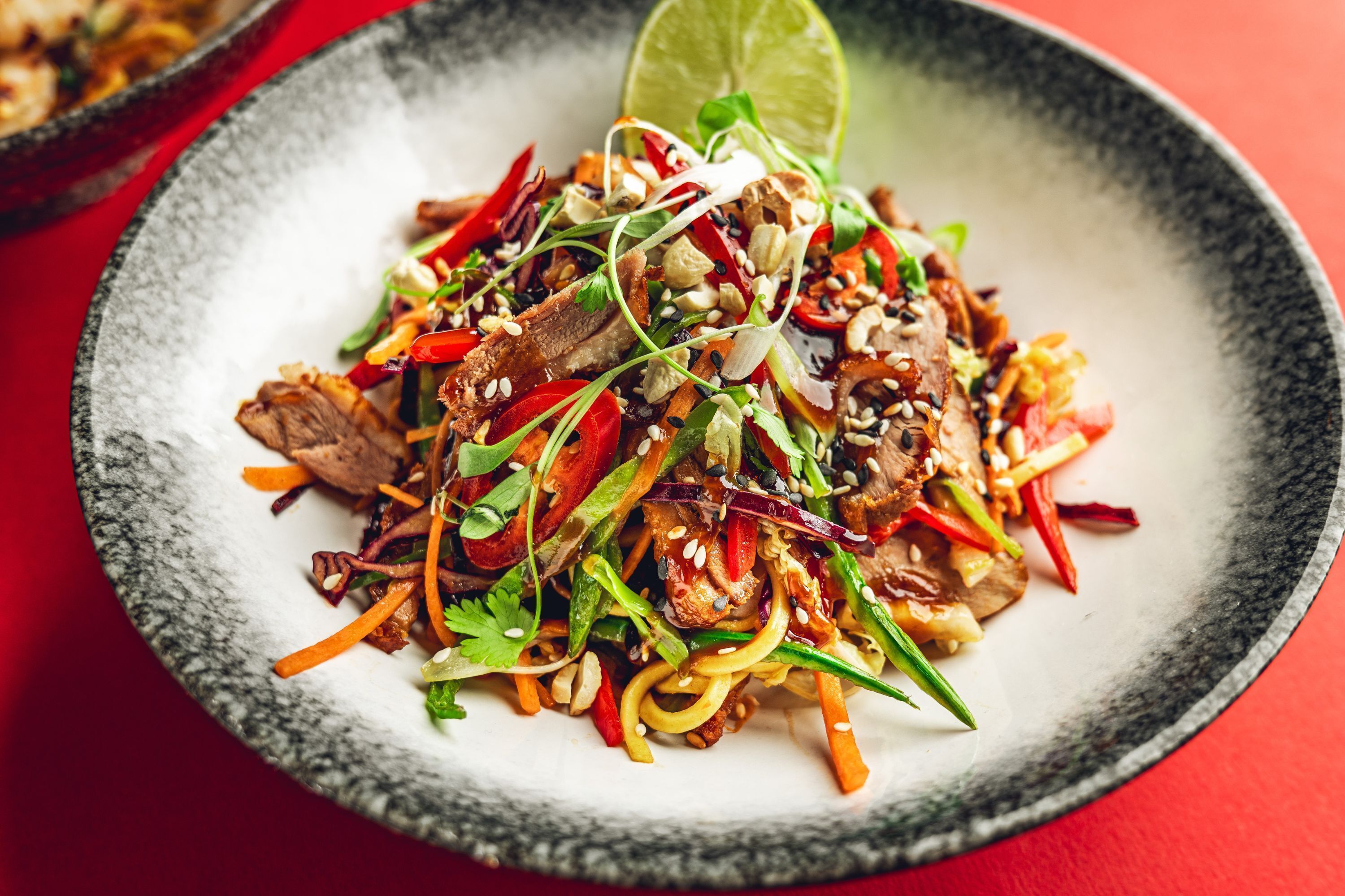 Un plato de vegetales salteados con carne, decorado con semillas de sésamo y una cuña de lima.