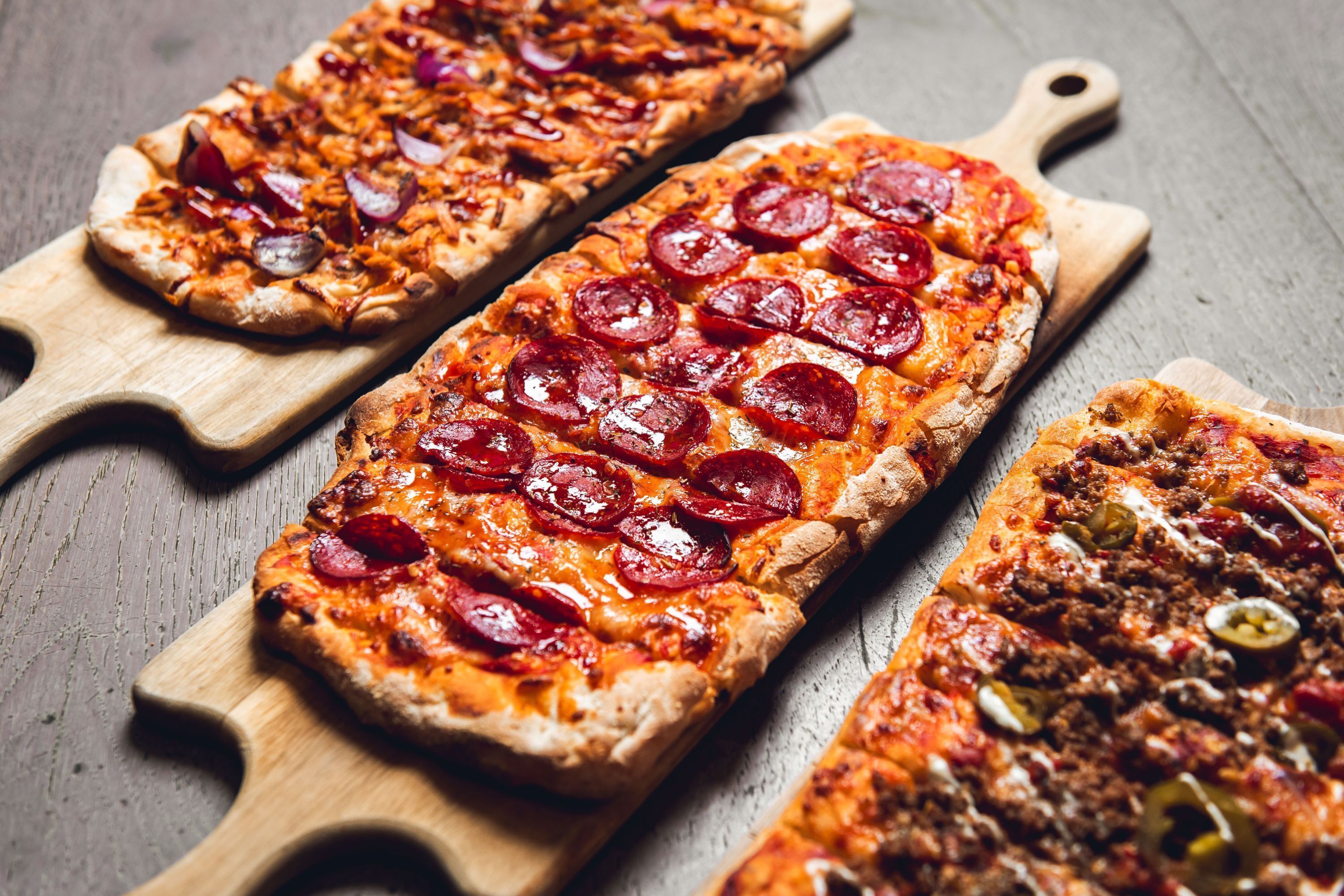 Trois pizzas rectangulaires servies sur des planches en bois.