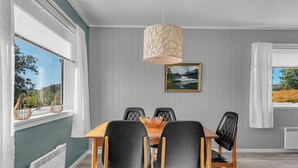 A dining area with a wooden table, black chairs, a hanging light fixture, and a framed landscape painting on the wall.