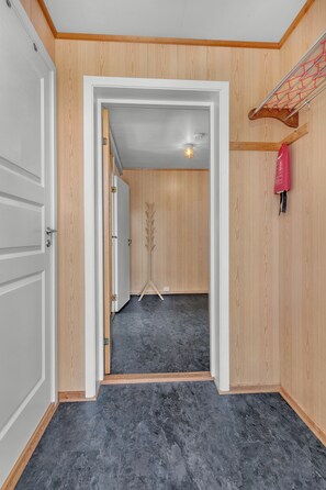 A hallway with wooden walls, a grey floor, and a door leading to another room. - Northern Norway Hidden Gem. Whales · Lights · Midnight Sun · Lofoten (Nordland)