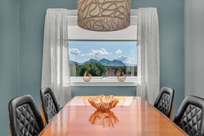 A dining area with a table and chairs, a window with a view of mountains, and a hanging light fixture.