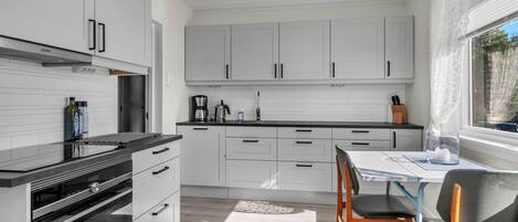 A modern kitchen with white cabinetry, a black countertop, and a dining area with a table and chairs.