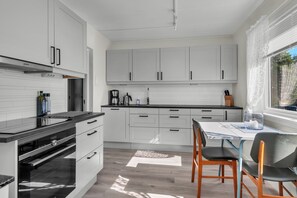 A modern kitchen with white cabinetry, a black countertop, and a dining area with a table and chairs. - Northern Norway Hidden Gem. Whales · Lights · Midnight Sun · Lofoten (Nordland)