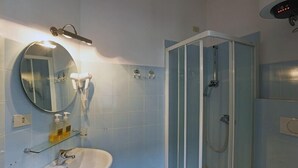 A bathroom with a white sink, a round mirror, a glass-enclosed shower, and a glass shelf with toiletries. - Sant Agostino Rooms (Milan)