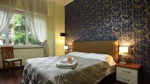 A hotel room with a bed, a chair, a nightstand with a lamp, and a window with curtains. - Sant Agostino Rooms (Milan)
