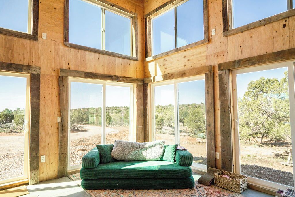 A room with a green sofa, large windows, and a view of a natural landscape.