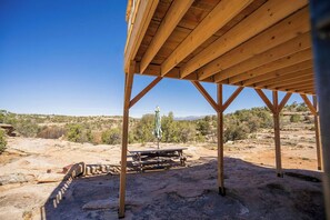 Eine Holzhütte mit Picknicktisch und Sonnenschirm vor einer Wüstenlandschaft.