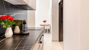 A modern kitchen with black countertops, a built-in stove, and a dining area with a small table and chairs. - Luxury Apartment in Nice Plage (Nice)