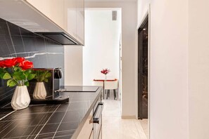 A modern kitchen with black countertops, a built-in stove, and a dining area with a small table and chairs. - Luxury Apartment in Nice Plage (Nice)