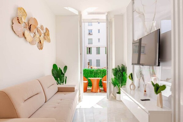 A modern living room with a sofa, a flat-screen TV, and decorative wall art. - Luxury Apartment in Nice Plage (Nice)