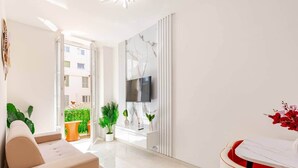 A modern living room with a sofa, a TV mounted on a wall, and a balcony with plants. - Luxury Apartment in Nice Plage (Nice)
