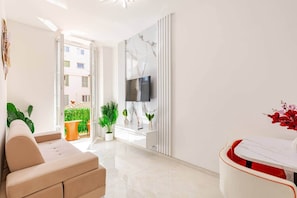 A modern living room with a sofa, a TV mounted on a wall, and a balcony with plants. - Luxury Apartment in Nice Plage (Nice)