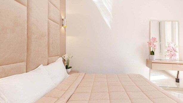 A bedroom with a large bed, a nightstand with a vase of flowers, and a mirror above a vanity. - Luxury Apartment in Nice Plage (Nice)