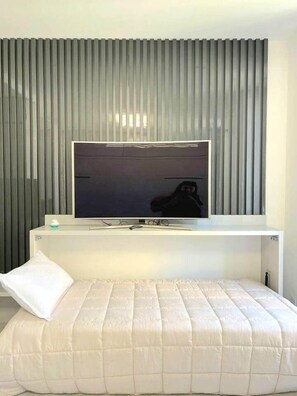 Ein modernes Schlafzimmer mit einem großen Bett, einem Wandfernseher und einer Wand mit vertikalen Jalousien.