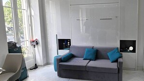 A modern interior with a grey sofa, teal cushions, a window with a view, and a door with a handle.