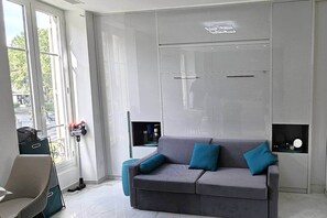 A modern interior with a grey sofa, teal cushions, a window with a view, and a door with a handle.