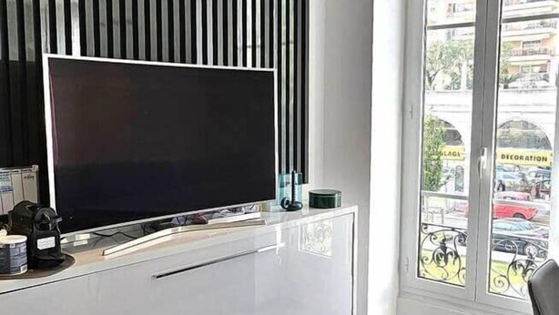 A modern living room with a large flat-screen TV, a sleek black entertainment unit, and a glass door leading to an outdoor area.