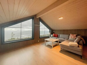 A spacious loft bedroom with large windows, a wooden ceiling, and a cozy seating area with a sofa and a coffee table. - Modern cabin with panoramic views in Vrådal (Vrådal)