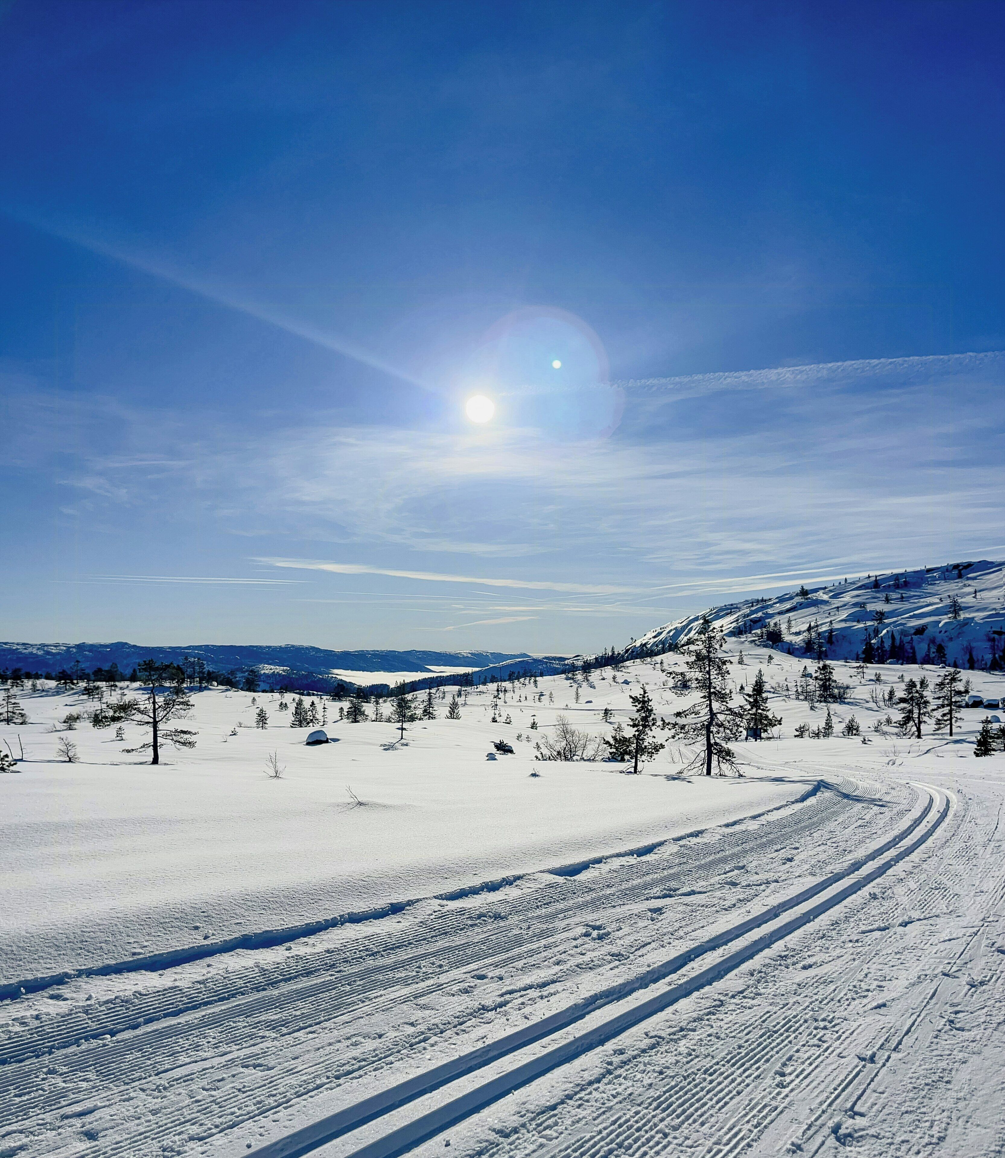 Un paisaje nevado con cielo despejado, el sol y una pista de esquí.