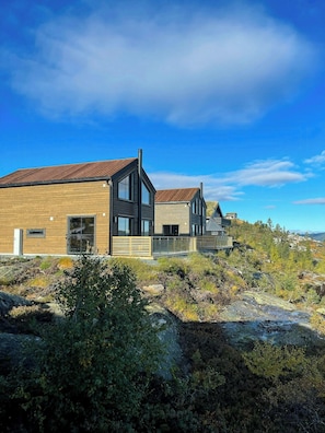 A modern two-story house with a wooden facade and a metal roof, situated in a natural landscape with sparse vegetation. - Modern cabin with panoramic views in Vrådal (Vrådal)