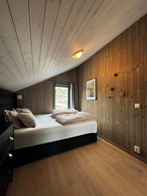 A bedroom with a wooden ceiling, a bed with pillows, a window, and a wall-mounted light fixture. - Modern cabin with panoramic views in Vrådal (Vrådal)
