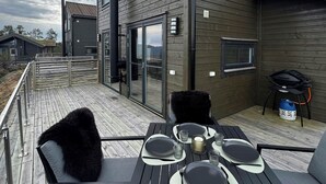 A modern outdoor dining area with a wooden deck, metal chairs, and a table set for four. - Modern cabin with panoramic views in Vrådal (Vrådal)