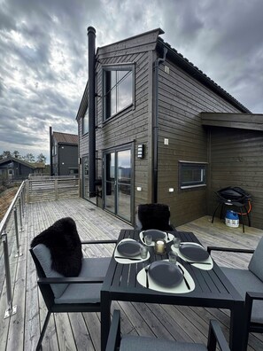 Ein moderner Essbereich im Freien mit einer Holzterrasse, Metallstühlen und einem Tisch für vier Personen.