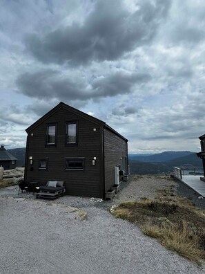 A dark wooden cabin with a small porch, a window, and a door. - Modern cabin with panoramic views in Vrådal (Vrådal)
