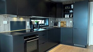 A modern kitchen with dark cabinetry, a built-in oven, and a wooden floor. - Modern cabin with panoramic views in Vrådal (Vrådal)