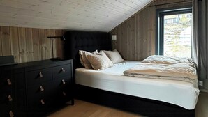 A bedroom with a sloped ceiling, a bed with a black headboard, a bedside table, and a dresser with drawers. - Modern cabin with panoramic views in Vrådal (Vrådal)