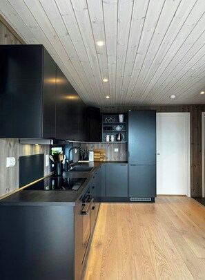 A modern kitchen with dark cabinetry, a wooden ceiling, and a built-in oven. - Modern cabin with panoramic views in Vrådal (Vrådal)
