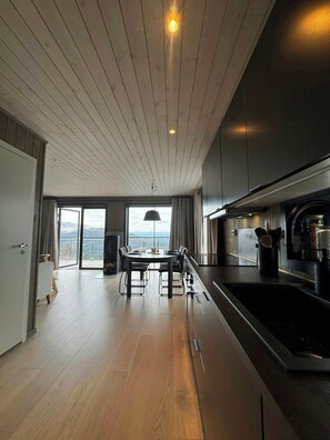 A modern kitchen with a central island, a dining area with a view, and a wooden ceiling. - Modern cabin with panoramic views in Vrådal (Vrådal)