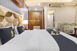 A hotel room with a large bed, a sofa, a desk with a kettle, and a mirror. - Royal Saffron by Stay Pattern- City Center (Srinagar)