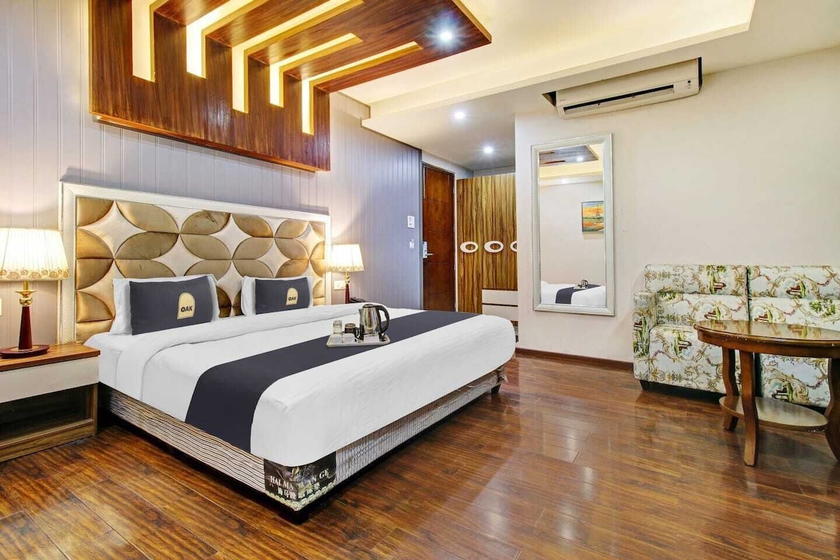 A hotel room with a large bed, a sofa, a small table, and a mirror.