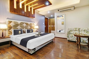 A hotel room with a large bed, a sofa, a small table, and a mirror. - Royal Saffron by Stay Pattern- City Center (Srinagar)