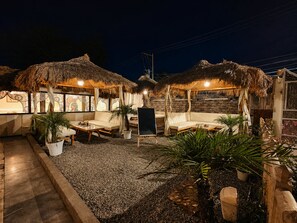 A nighttime outdoor seating area with thatched-roof structures, cushioned seating, and potted plants. - Royal Saffron by Stay Pattern- City Center (Srinagar)