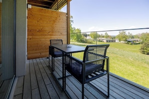 Un patio exterior con mesa y sillas de madera, vista a un paisaje verde y cielo despejado.