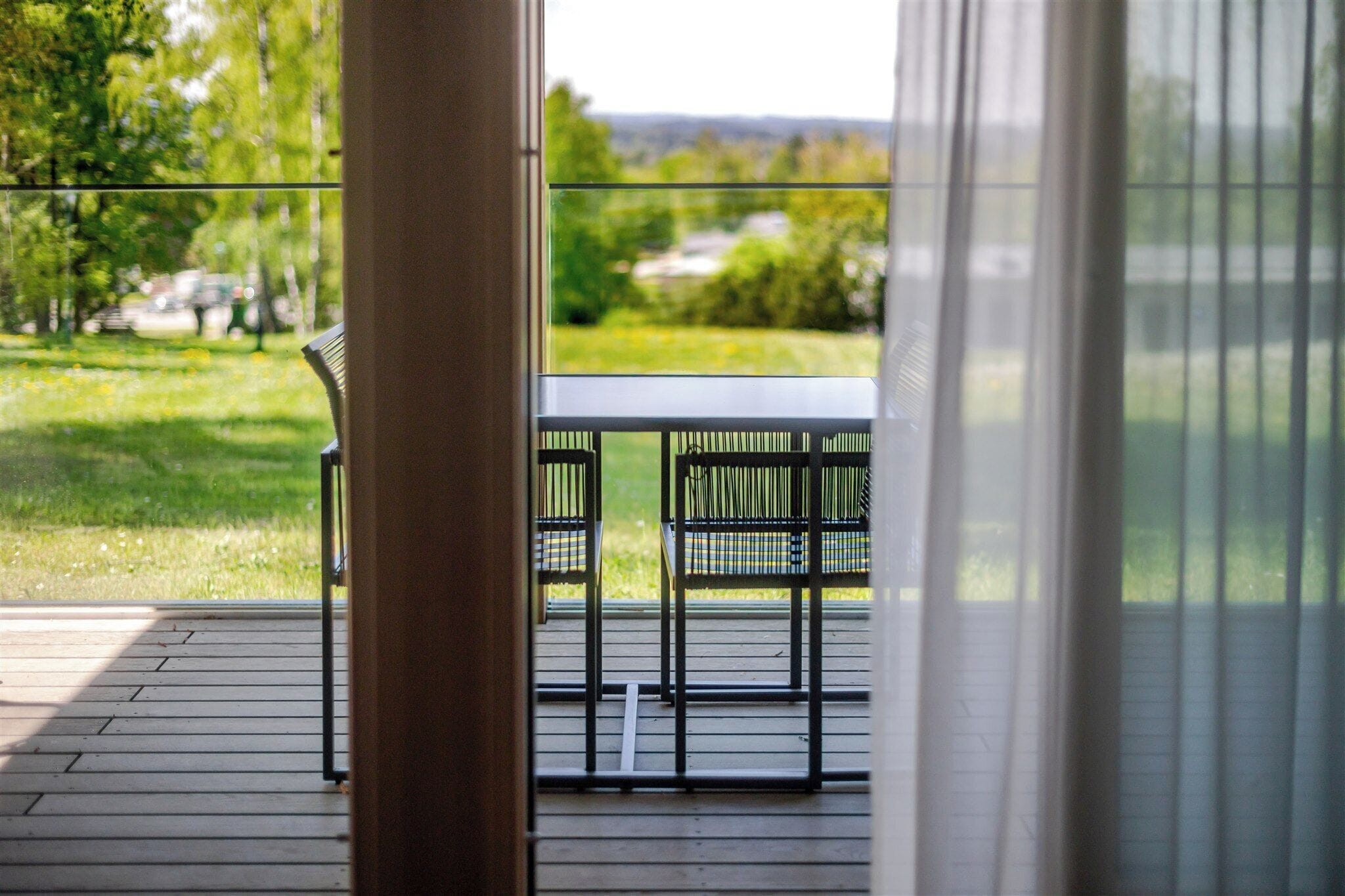 An outdoor patio with a table and chairs, a wooden deck, and a view of a green landscape.